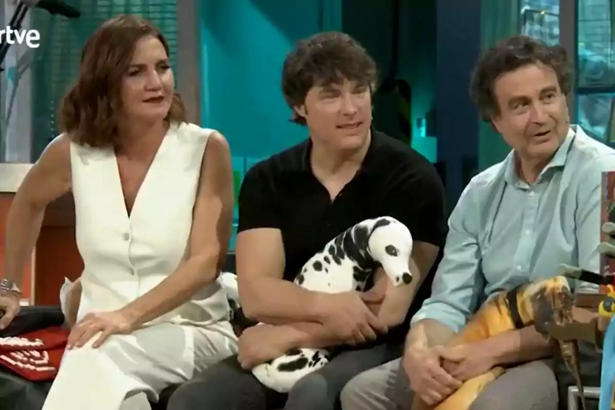 Pepe Rodríguez, Samantha Vallejo-Nágera y Jordi Cruz están sentadas en un set de La Revuelta, una mujer lleva un vestido blanco y los dos hombres a su lado sostienen peluches de animales.