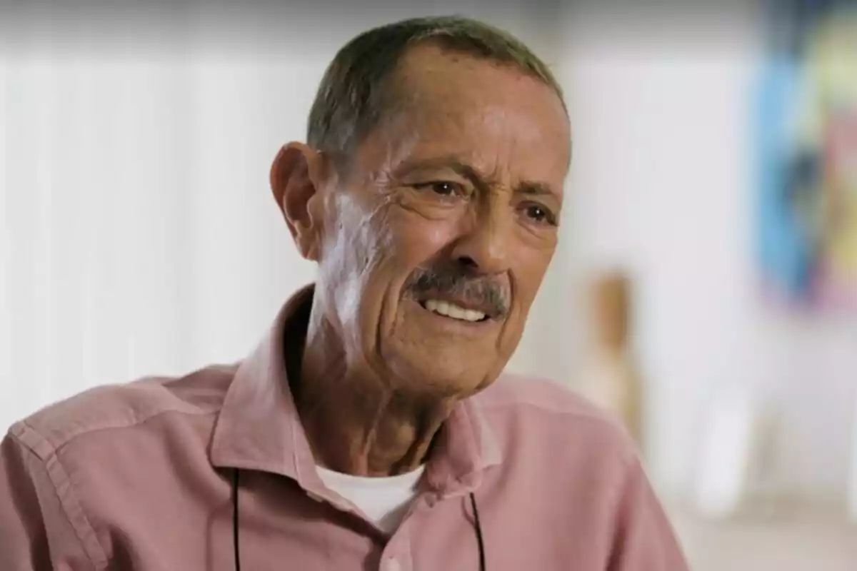 Julián Muñoz llorando con camisa rosa y bigote sentado en un entorno interior.