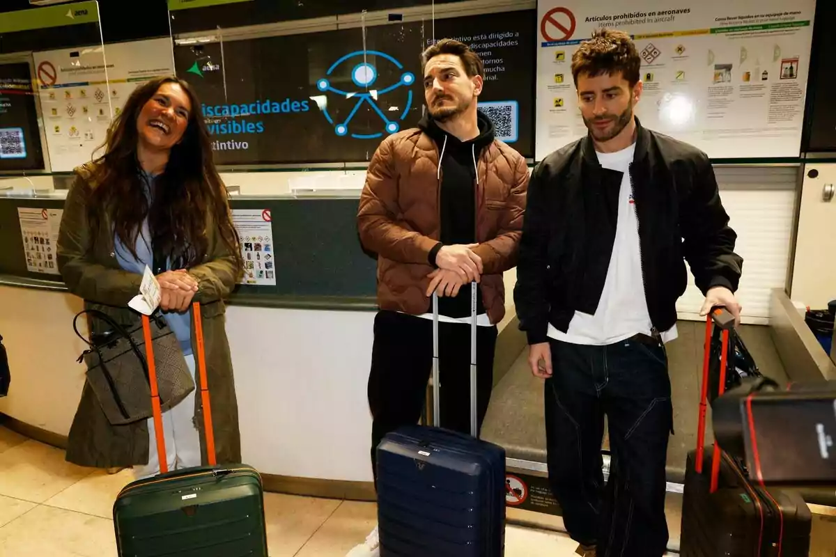 Tres personas como Laura Cuevas, Damián Quintero y Pelayo Díaz sonríen mientras sostienen sus maletas en un área de aeropuerto, con señales y carteles informativos en el fondo camino a Supervivientes. Tres personas como Laura Cuevas, Damián Quintero y Pelayo Díaz sonríen mientras sostienen sus maletas en un área de aeropuerto, con señales y carteles informativos en el fondo camino a Supervivientes.