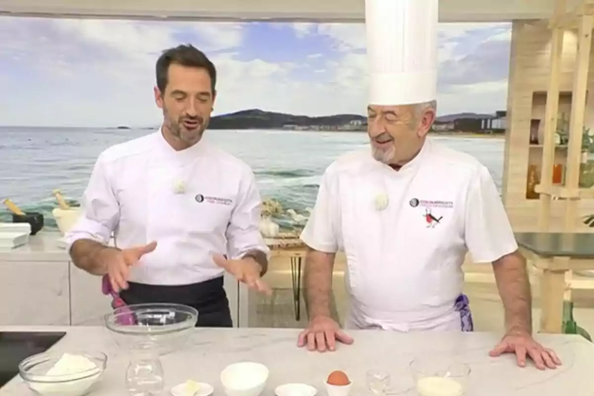 Karlos Argüiñano y Joseb Argüiñanos en una cocina con vista al mar, preparando ingredientes sobre una mesa en Cocina Abierta. Karlos Argüiñano y Joseb Argüiñanos en una cocina con vista al mar, preparando ingredientes sobre una mesa en Cocina Abierta.