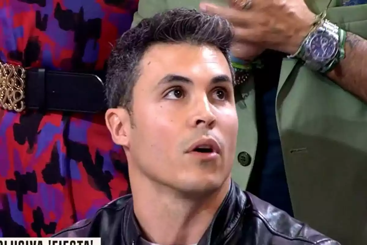 Kiko Jiménez con chaqueta de cuero mira hacia arriba mientras otra persona con reloj y chaqueta verde está detrás en Fiesta. Kiko Jiménez con chaqueta de cuero mira hacia arriba mientras otra persona con reloj y chaqueta verde está detrás en Fiesta.