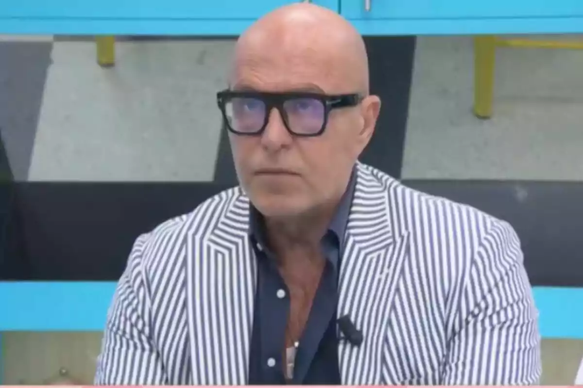 Kiko Matamoros calb amb ulleres i jaqueta de ratlles blanques i blaves assegut en un ambient interior a 'La família de la tele'.