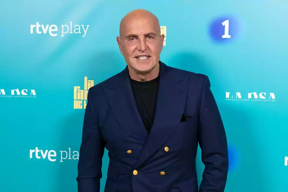 Kiko Matamoros calb amb una jaqueta blau marí i botons daurats posa davant d'un fons blau amb logotips de 