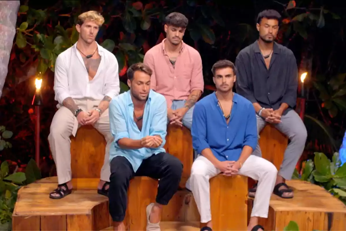 Cinco hombres sentados en un entorno al aire libre con vegetación de fondo, todos visten camisas de colores y pantalones claros, algunos con sandalias. Captura de 'La Isla de las Tentaciones' Cinco hombres sentados en un entorno al aire libre con vegetación de fondo, todos visten camisas de colores y pantalones claros, algunos con sandalias. Captura de 'La Isla de las Tentaciones'