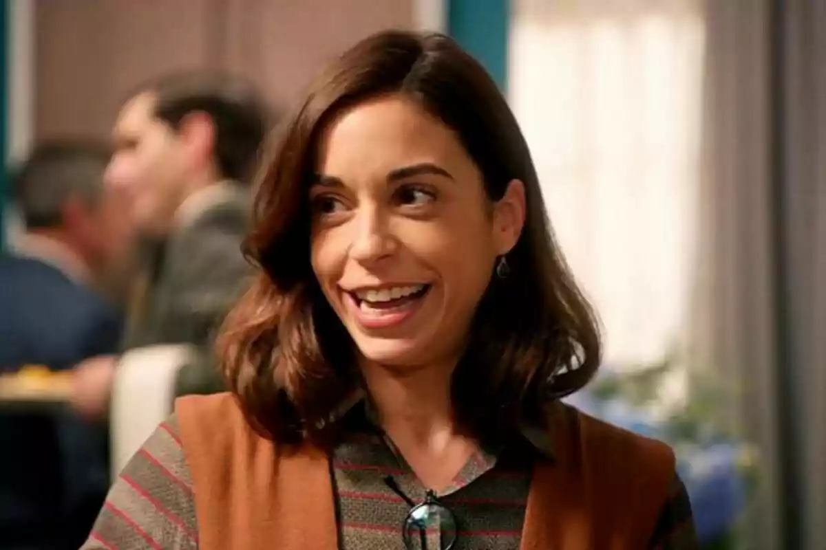 Celia sonriente con cabello castaño y una camisa a rayas, con personas desenfocadas en el fondo. Captura de 'La Moderna' Celia sonriente con cabello castaño y una camisa a rayas, con personas desenfocadas en el fondo. Captura de 'La Moderna'