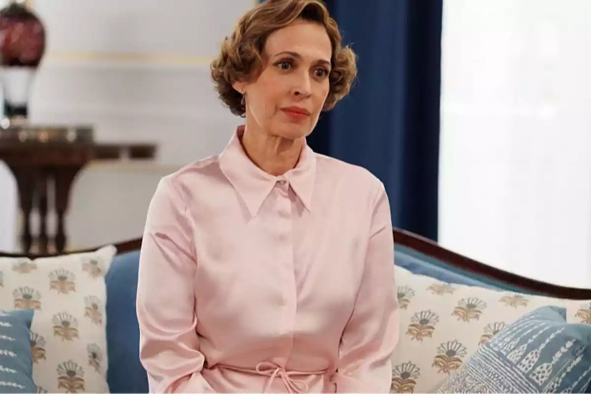 Maruja con cabello corto y ondulado sentada en un sofá con cojines decorativos y vistiendo una blusa rosa claro. Captura de 'La Moderna' Maruja con cabello corto y ondulado sentada en un sofá con cojines decorativos y vistiendo una blusa rosa claro. Captura de 'La Moderna'