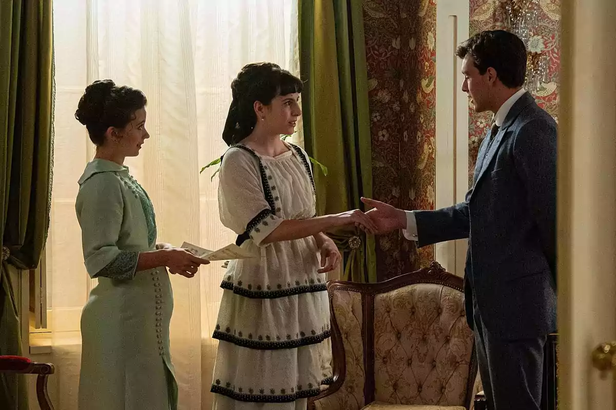 Julia con otras dos personas vestidas con ropa de época están en una habitación elegantemente decorada, dos mujeres y un hombre, una de las mujeres le da la mano al hombre mientras la otra sostiene un papel. Captura de 'La Promesa' Julia con otras dos personas vestidas con ropa de época están en una habitación elegantemente decorada, dos mujeres y un hombre, una de las mujeres le da la mano al hombre mientras la otra sostiene un papel. Captura de 'La Promesa'