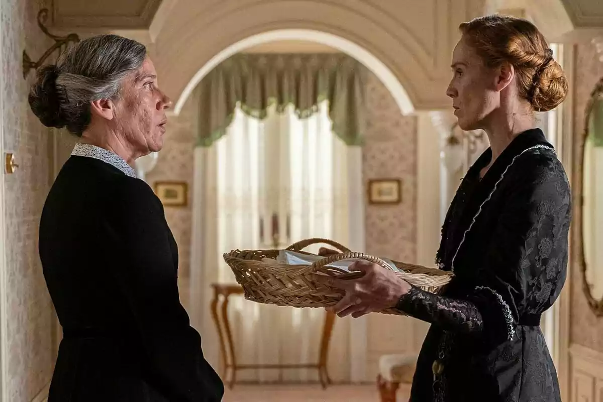 Petra y Pía vestidas de época conversan en un elegante interior mientras una de ellas sostiene una canasta. Captura de 'La Promesa' Petra y Pía vestidas de época conversan en un elegante interior mientras una de ellas sostiene una canasta. Captura de 'La Promesa'