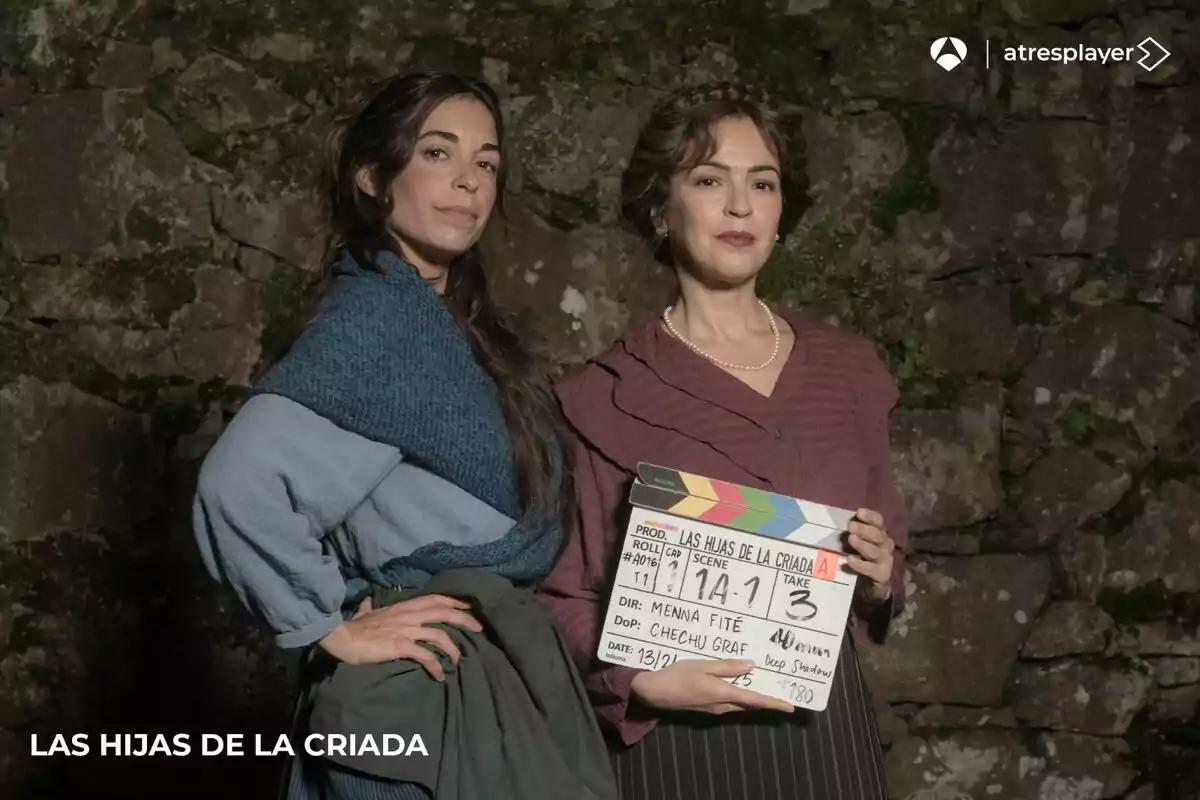 Veronica Sánchez y Carlota Baró posan frente a una pared de piedra, una de ellas sostiene una claqueta de cine que indica detalles de la producción Veronica Sánchez y Carlota Baró posan frente a una pared de piedra, una de ellas sostiene una claqueta de cine que indica detalles de la producción