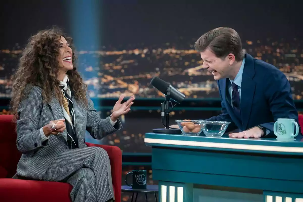 Rosario Flores y Marc Giró riendo durante una entrevista en Late Xou con Marc Giró, con una ciudad iluminada de fondo. Rosario Flores y Marc Giró riendo durante una entrevista en Late Xou con Marc Giró, con una ciudad iluminada de fondo.