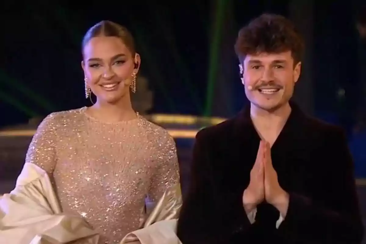 Dues persones somrients en un escenari, una és Laura Escanes amb un vestit brillant i l'altra és Miki Núñez amb un vestit fosc.