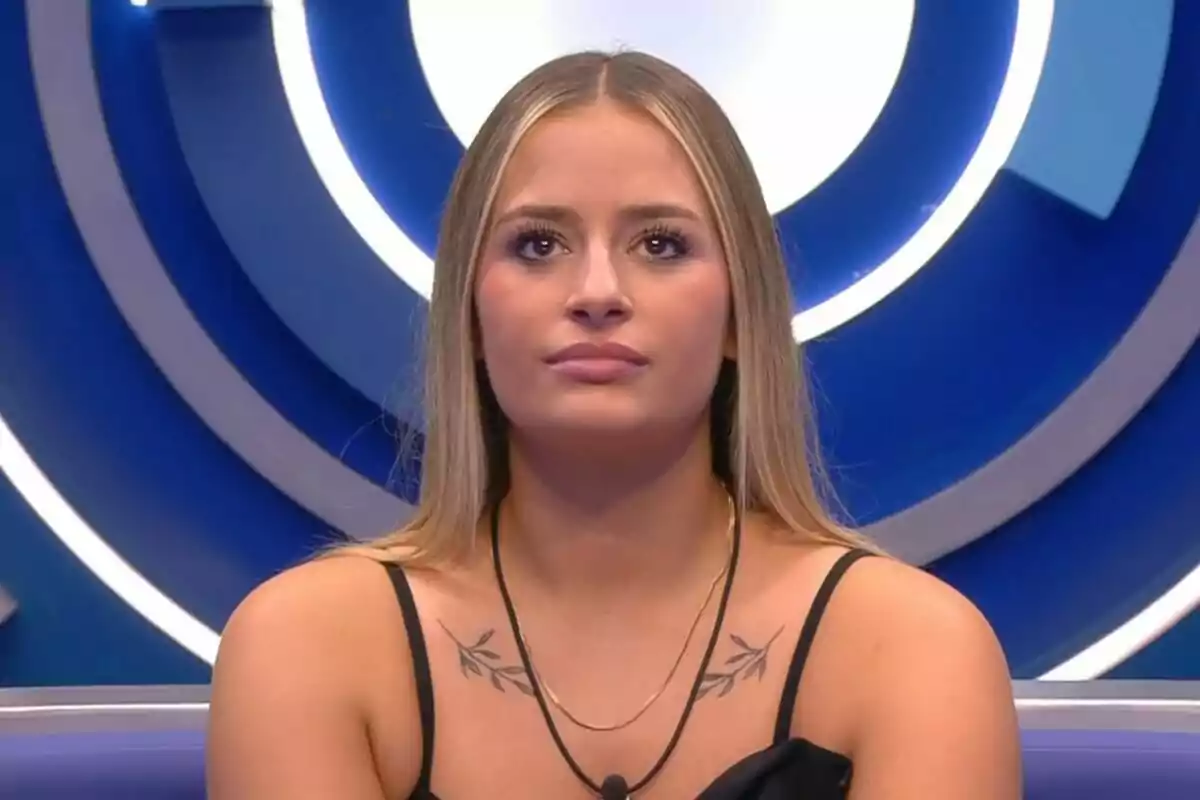 Plano corto de Laura Galera con cara seria sentada frente a un fondo azul con círculos iluminados. Plano corto de Laura Galera con cara seria sentada frente a un fondo azul con círculos iluminados.