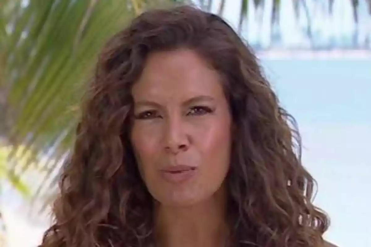 Laura Madrueño amb cabell arrissat i expressió seriosa en un entorn tropical amb palmeres i el mar de fons a Supervivientes.