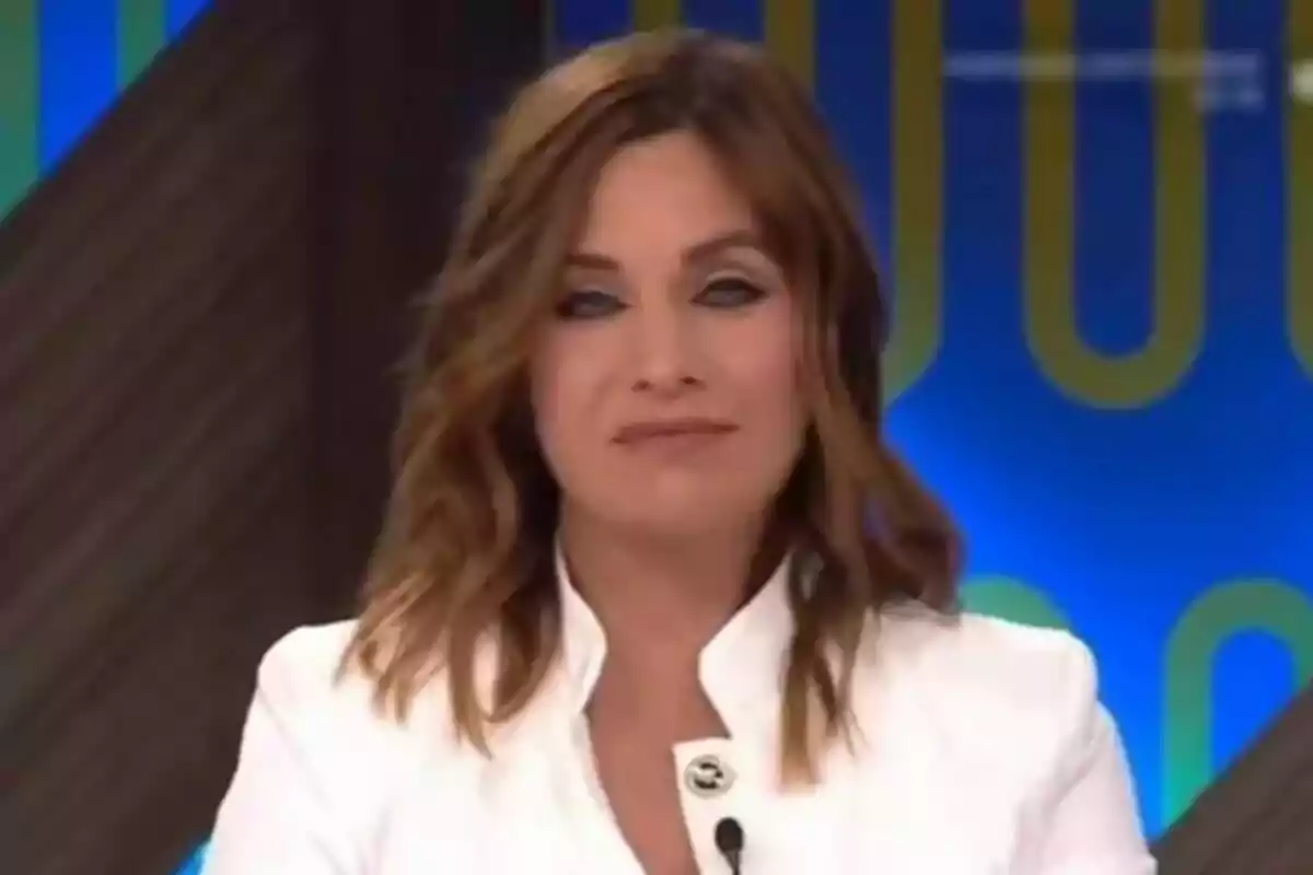 Leire Martínez con cabello castaño y ondulado lleva una chaqueta blanca y está frente a un fondo azul con detalles amarillos. Leire Martínez con cabello castaño y ondulado lleva una chaqueta blanca y está frente a un fondo azul con detalles amarillos.