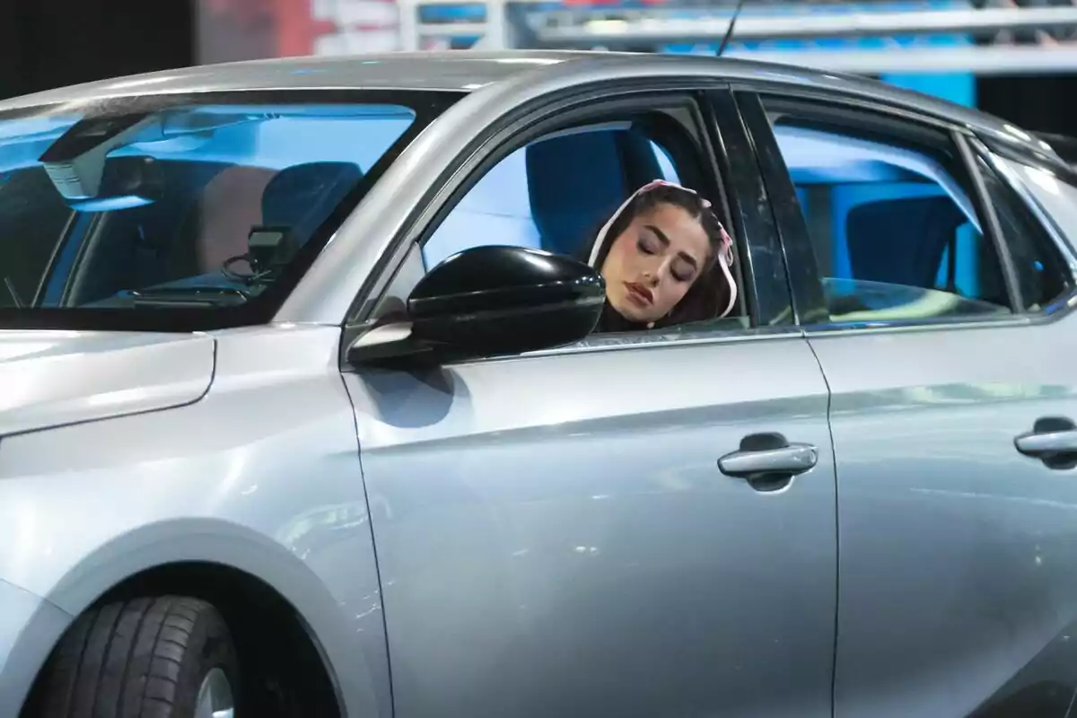 Lola Lolita con los ojos cerrados está sentada en el asiento del conductor de un automóvil plateado en El Desafío. Lola Lolita con los ojos cerrados está sentada en el asiento del conductor de un automóvil plateado en El Desafío.