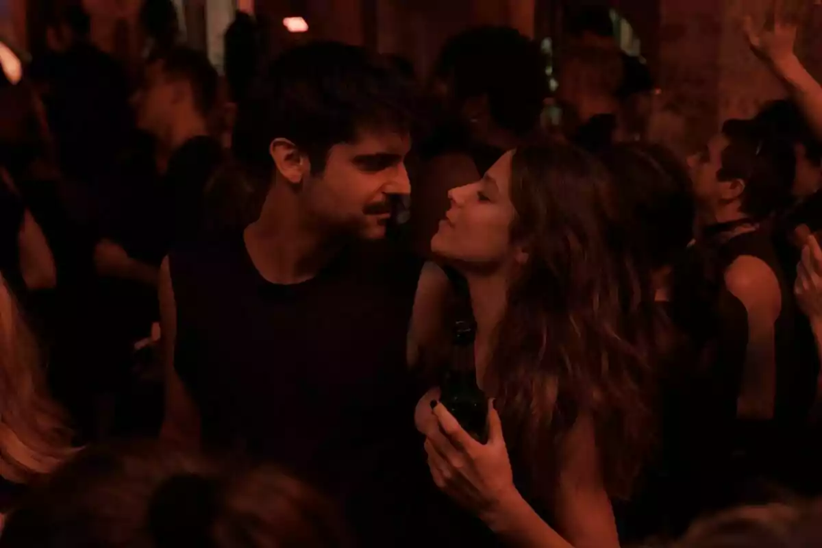 Una pareja formada por Iria del Río y Francesco Carril se mira intensamente mientras baila en un club lleno de gente, con luces tenues y ambiente festivo en la serie Los Años Nuevos. Una pareja formada por Iria del Río y Francesco Carril se mira intensamente mientras baila en un club lleno de gente, con luces tenues y ambiente festivo en la serie Los Años Nuevos.