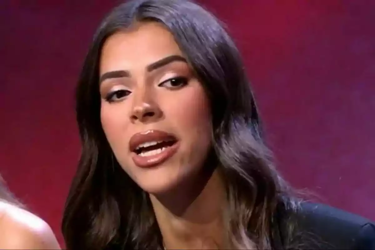 Lluïa amb cabell llarg i fosc parlant davant d'un fons vermell a Gran Hermano. Lluïa amb cabell llarg i fosc parlant davant d'un fons vermell a Gran Hermano.
