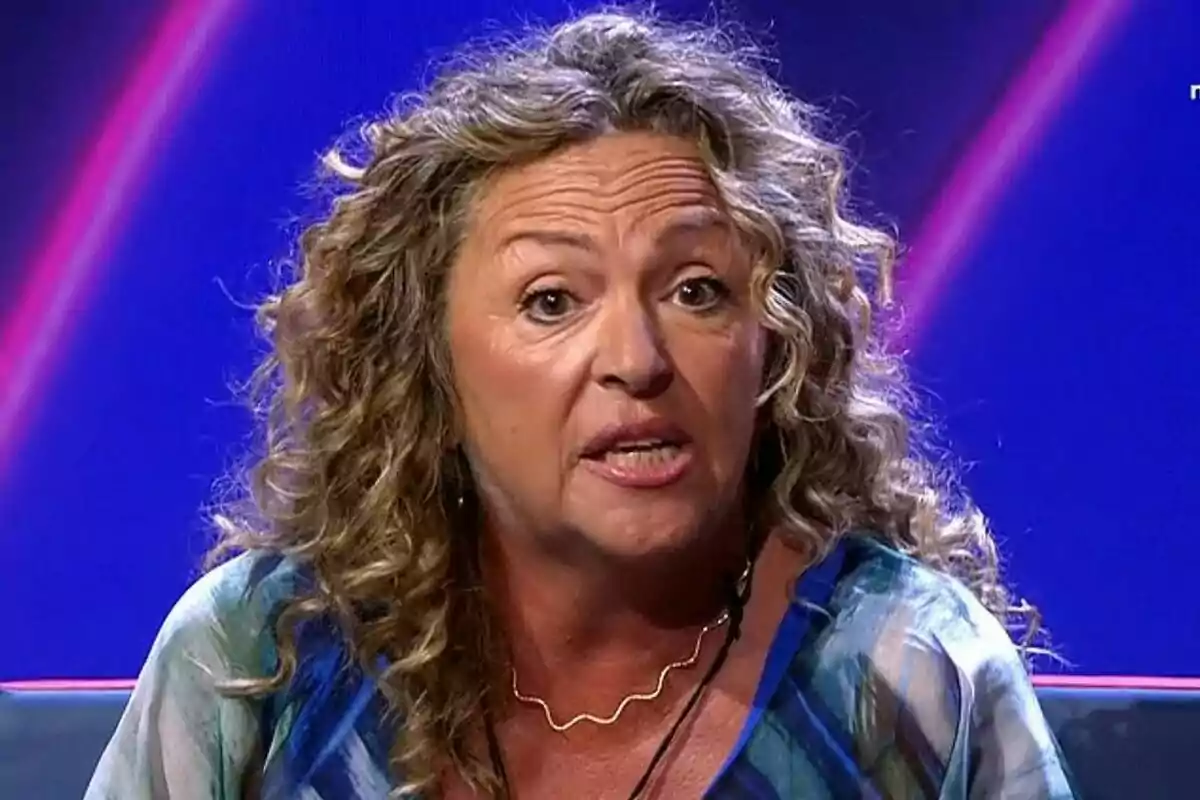 La madre de Juan con cabello rizado y expresión seria en el plató de Gran Hermano con fondo azul. La madre de Juan con cabello rizado y expresión seria en el plató de Gran Hermano con fondo azul.