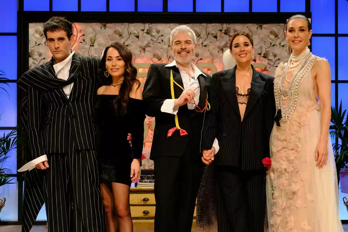 Palomo Spain, María Escoté, Lorenzo Caprile, Adriana Ugarte i Raquel Sánchez Silva posant juntes en un escenari amb fons floral i llums blaves, algunes vesteixen vestits elegants i altres roba formal a Maestros de la Costura.