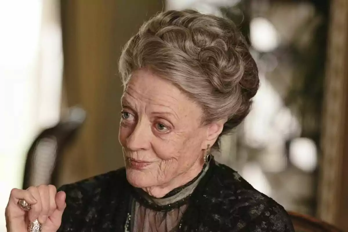 Maggie Smith amb els cabells canosos recollits i expressió pensativa, vestida amb roba elegant i fosca. Maggie Smith amb els cabells canosos recollits i expressió pensativa, vestida amb roba elegant i fosca.