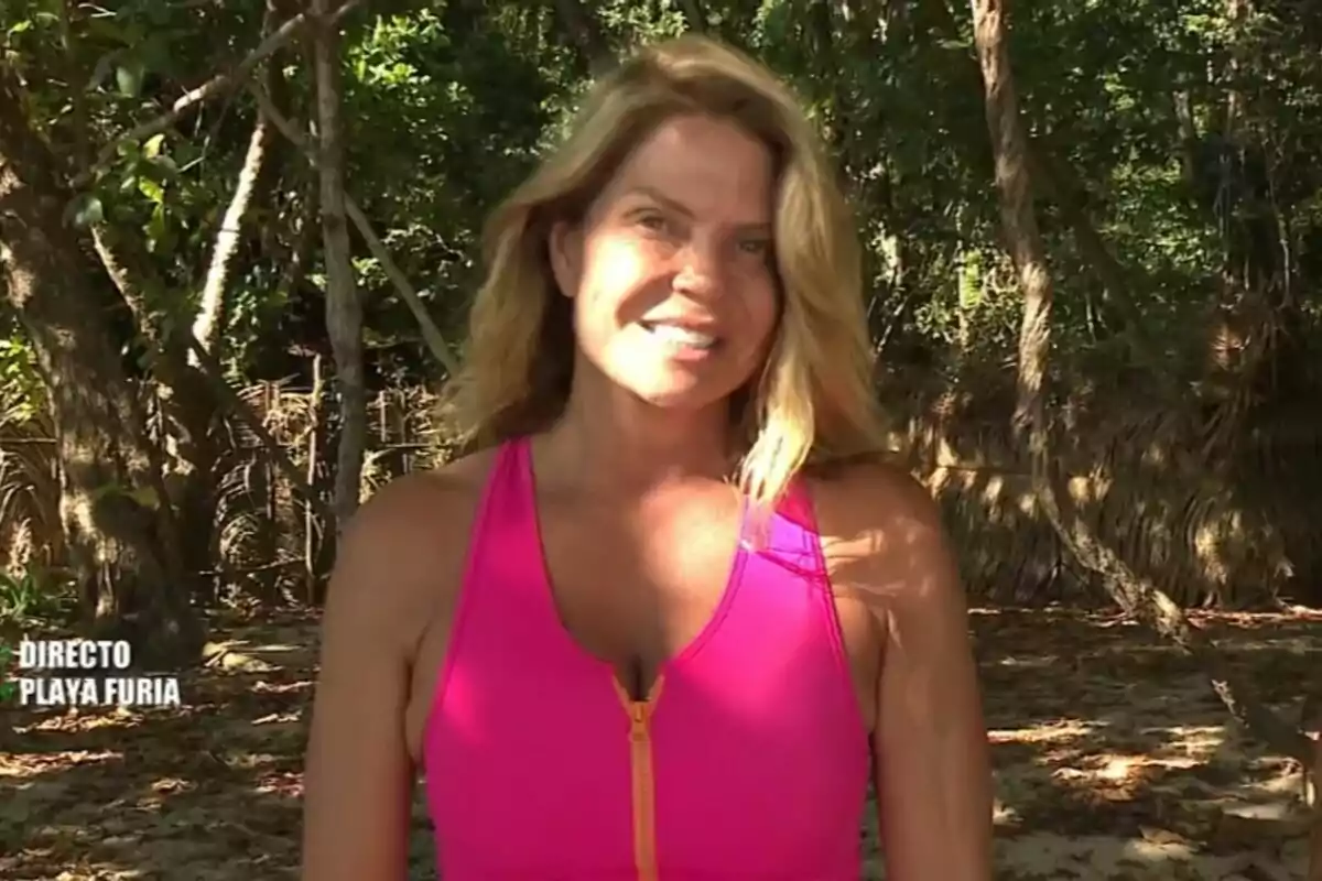 Makoke con una camiseta rosa está de pie en un entorno natural con árboles y sombra en Supervivientes. Makoke con una camiseta rosa está de pie en un entorno natural con árboles y sombra en Supervivientes.