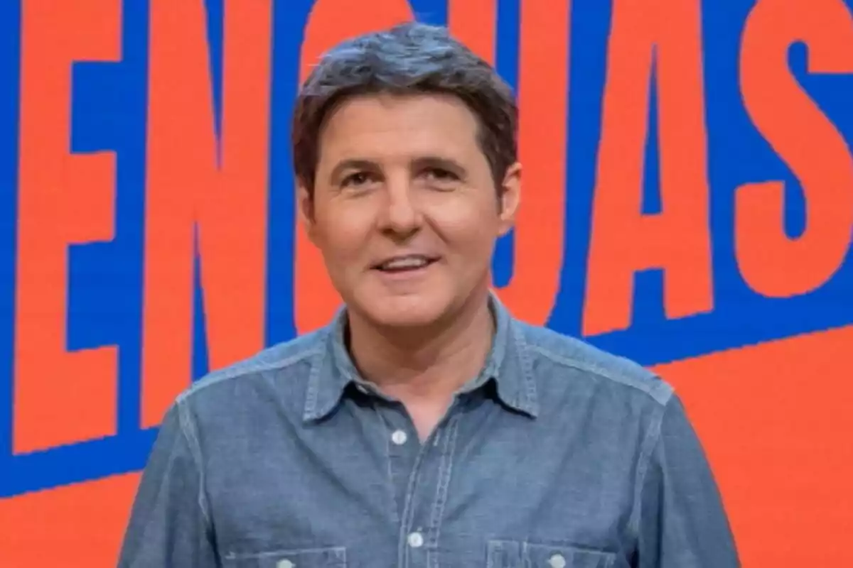 Jesús Cintora con camisa de mezclilla frente a un fondo con letras grandes en colores azul y naranja de Malas Lenguas.