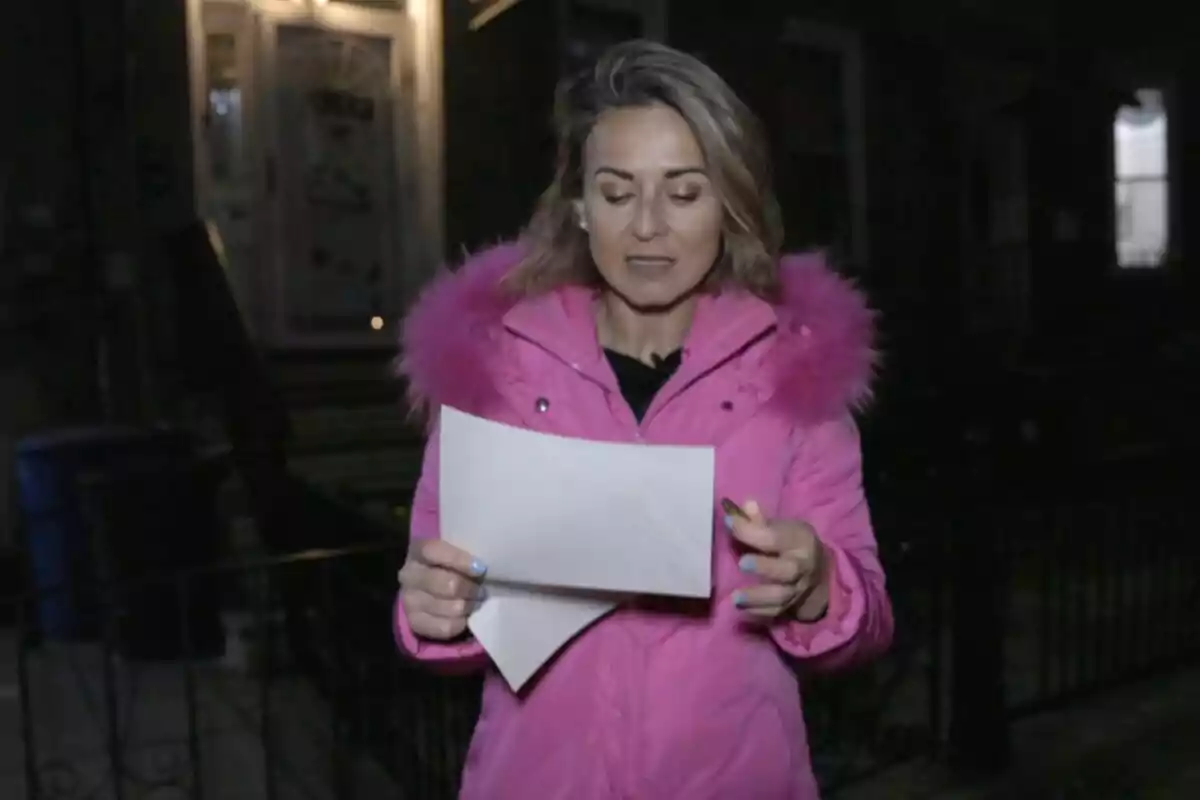 Mamen Salas con abrigo rosa sostiene una hoja de papel mientras está de pie frente a una casa de noche en 'Cuarto Milenio'.