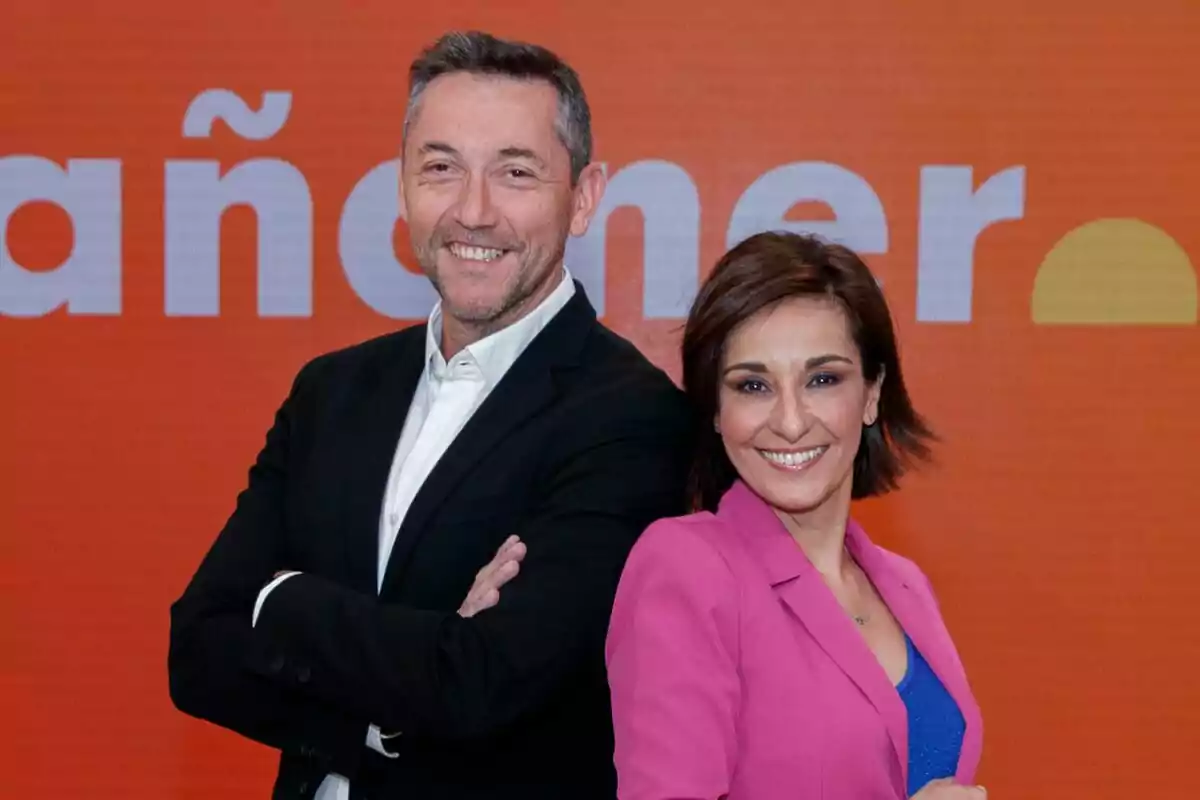 Javier Ruiz y Adela González sonrientes posan frente a un fondo naranja con texto parcialmente visible de Mañanaeors. Javier Ruiz y Adela González sonrientes posan frente a un fondo naranja con texto parcialmente visible de Mañanaeors.