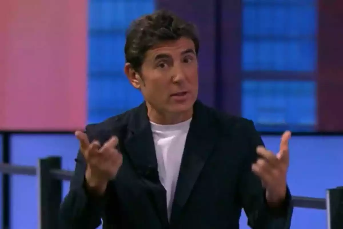 Manel Fuentes amb jaqueta fosca i samarreta blanca gesticula amb les mans en un entorn d'estudi amb fons blau i rosa a ¡Salta!. Manel Fuentes amb jaqueta fosca i samarreta blanca gesticula amb les mans en un entorn d'estudi amb fons blau i rosa a ¡Salta!.