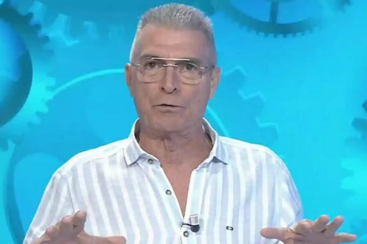 Manolo Sarria con camisa de rayas y gafas habla frente a un fondo azul con engranajes en Atrápame si puedes. Manolo Sarria con camisa de rayas y gafas habla frente a un fondo azul con engranajes en Atrápame si puedes.