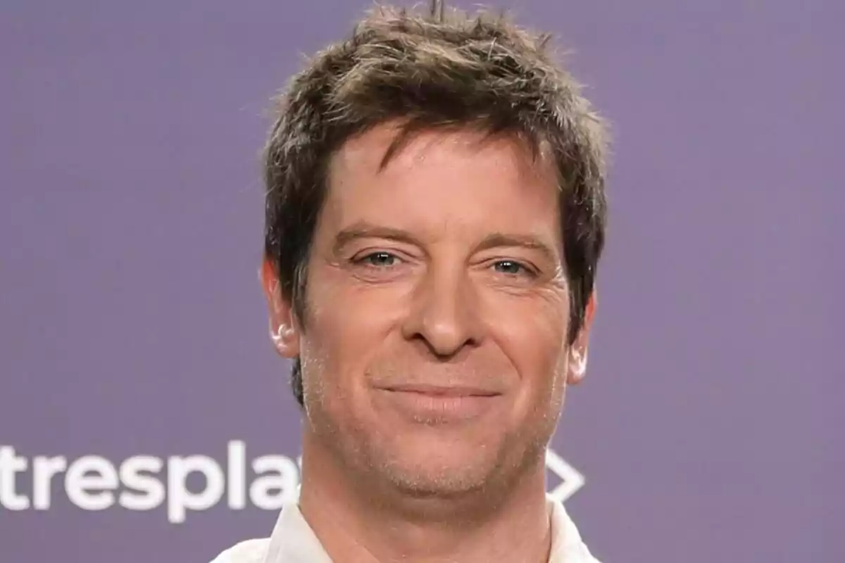 Manu Baqueiro amb cabell castany i expressió somrient davant d'un fons morat a Tu Cara Me Suena.
