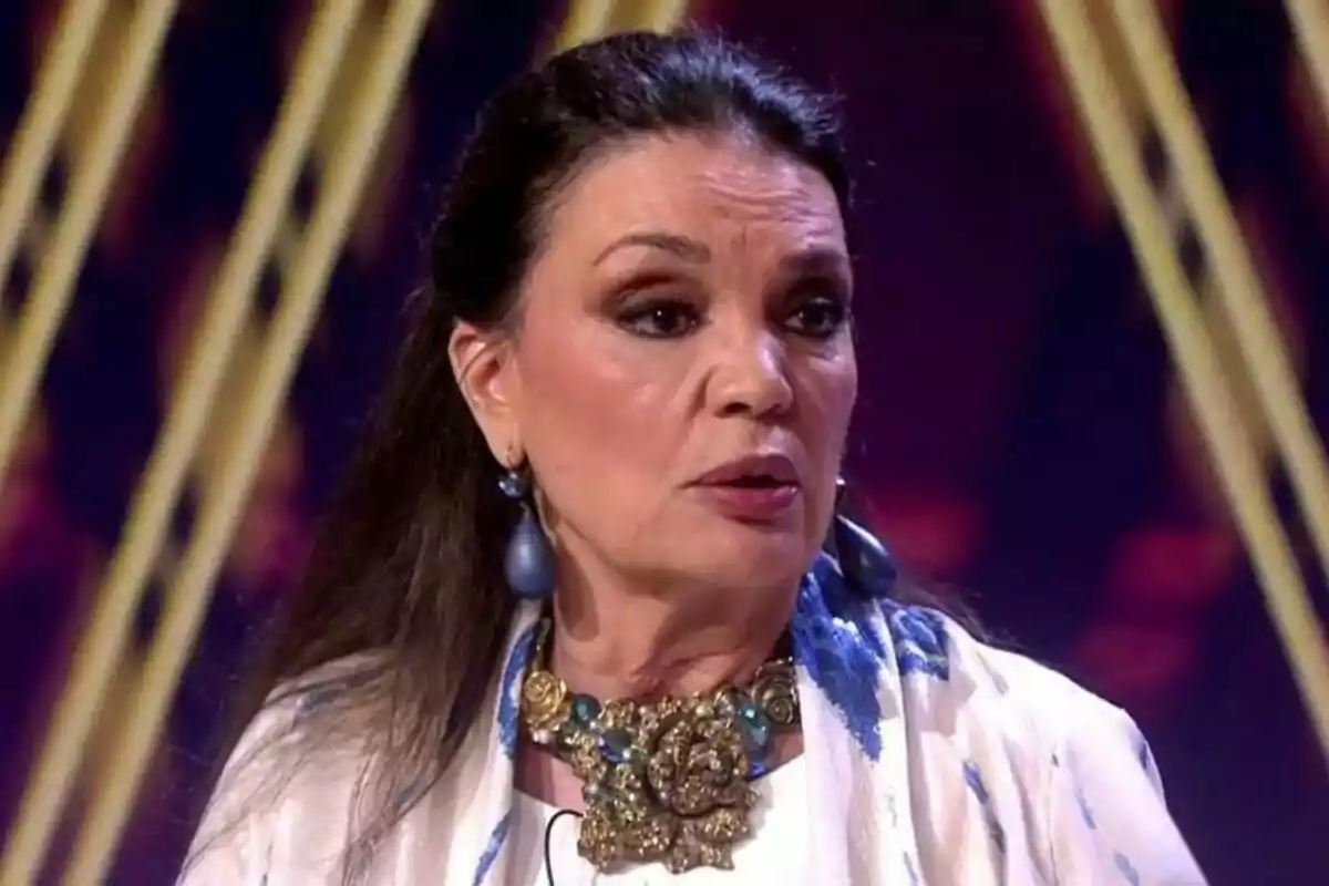María José Cantudo amb cabell fosc i solt, portant un collaret gran i arracades, està en un escenari amb llums de fons a De Viernes.