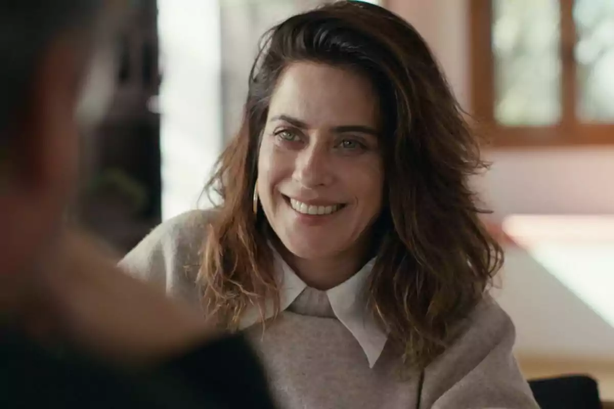 María León sonriendo con cabello castaño y suelto, vistiendo un suéter beige y camisa blanca, en un ambiente interior iluminado en Lo de Évole.