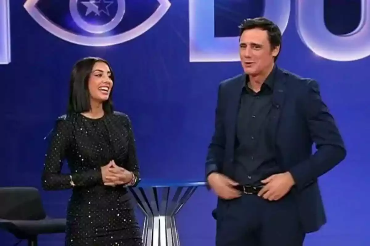 Ion Aramendi y Marieta Díaz sonríen en un escenario con fondo azul y un logotipo de ojo de GH DÚO. Ion Aramendi y Marieta Díaz sonríen en un escenario con fondo azul y un logotipo de ojo de GH DÚO.