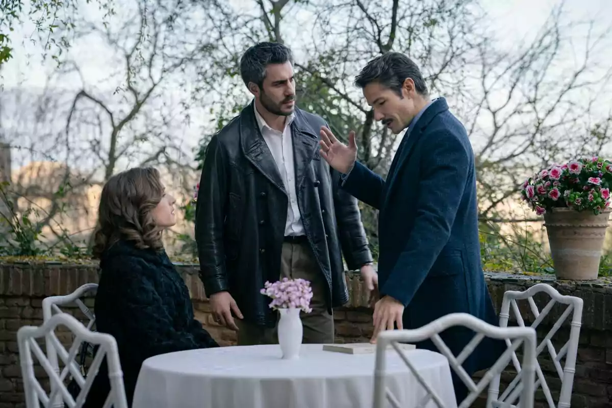 Marta Belmonte, Dani Tatay i Alejandro Albarracín interactuen en una terrassa amb una taula rodona i flors, dos homes drets conversen mentre una dona està asseguda a Sueños de Libertad. Marta Belmonte, Dani Tatay i Alejandro Albarracín interactuen en una terrassa amb una taula rodona i flors, dos homes drets conversen mentre una dona està asseguda a Sueños de Libertad.