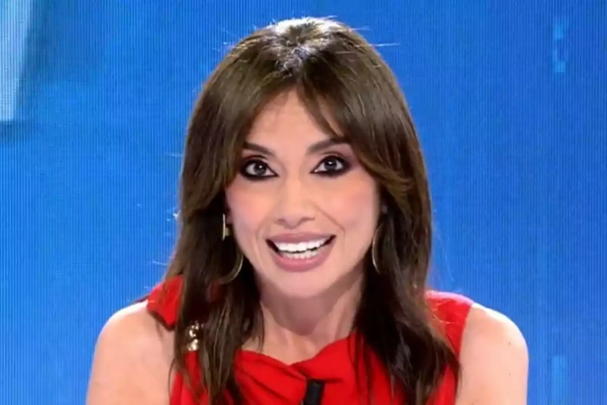 Marta Flich de cabells castanys somrient amb vestit vermell a Todo es Mentira davant d’un fons blau