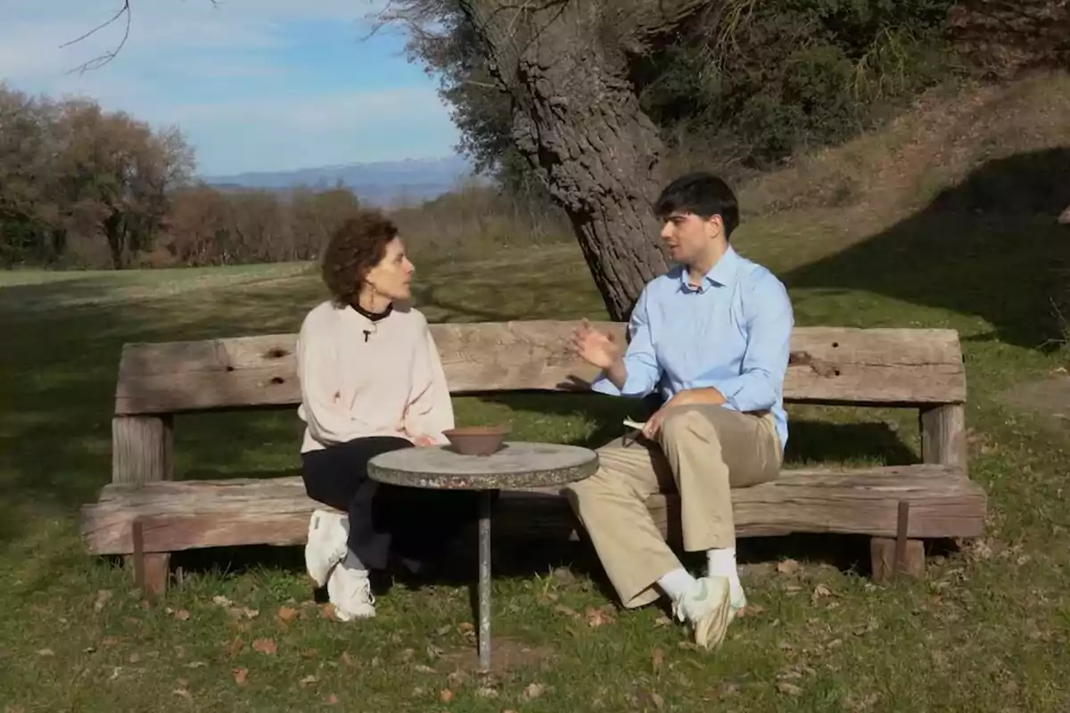 Marta Marco y Jon García sentadas en un banco de madera al aire libre conversan junto a una mesa pequeña en un entorno natural con árboles y césped en Off The Rec.