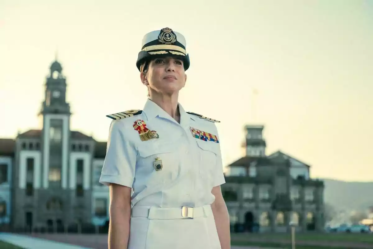Lucía Jiménez en uniforme naval blanco con insignias y gorra de oficial, de pie frente a un edificio histórico en Marusía. Vientos de Honor.