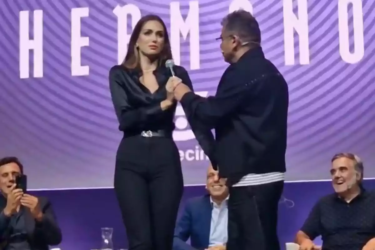 Maika i Jorge Javier Vázquez estan en un escenari, l'home sosté un micròfon mentre la dona sembla sorpresa, al fons hi ha persones assegudes i un cartell amb lletres grans a la roda de premsa de Gran Hermano Maika i Jorge Javier Vázquez estan en un escenari, l'home sosté un micròfon mentre la dona sembla sorpresa, al fons hi ha persones assegudes i un cartell amb lletres grans a la roda de premsa de Gran Hermano