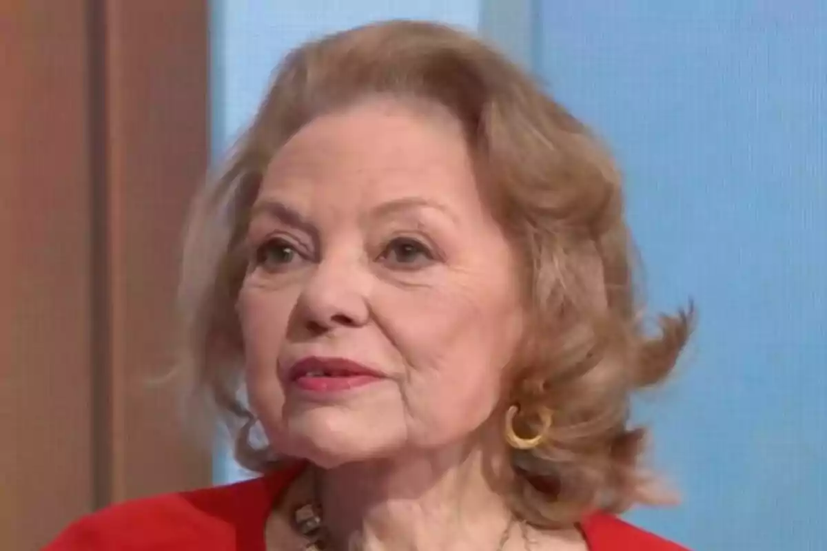 Mayra Gómez Kemp con cabello rubio y rizado, usando un pendiente dorado y un collar, vestida con una prenda roja, en un entorno interior en Mañaneros. Mayra Gómez Kemp con cabello rubio y rizado, usando un pendiente dorado y un collar, vestida con una prenda roja, en un entorno interior en Mañaneros.