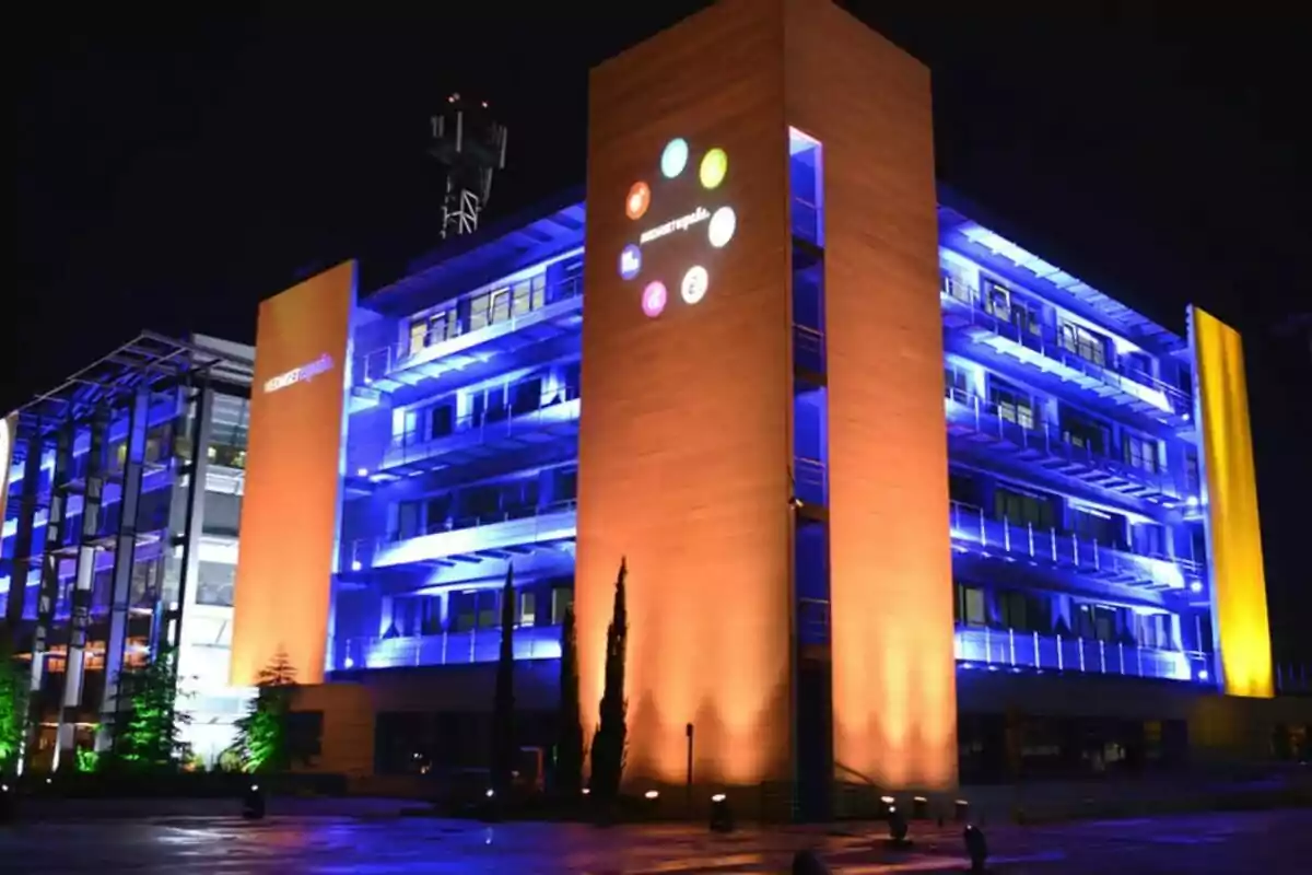 Edificio de Mediaest iluminado con luces azules y naranjas durante la noche.