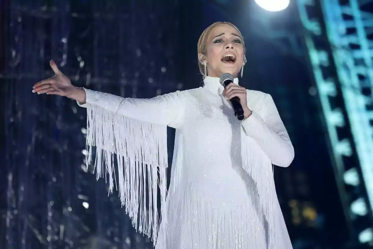 Melani cantant en un escenari amb un vestit blanc amb serrells a Tu Cara Me Suena.
