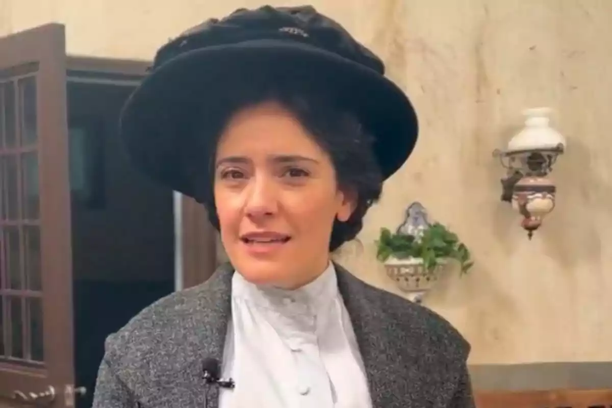 Melania Cruz con vestimenta de época y sombrero oscuro en un ambiente interior en La Promesa. Melania Cruz con vestimenta de época y sombrero oscuro en un ambiente interior en La Promesa.