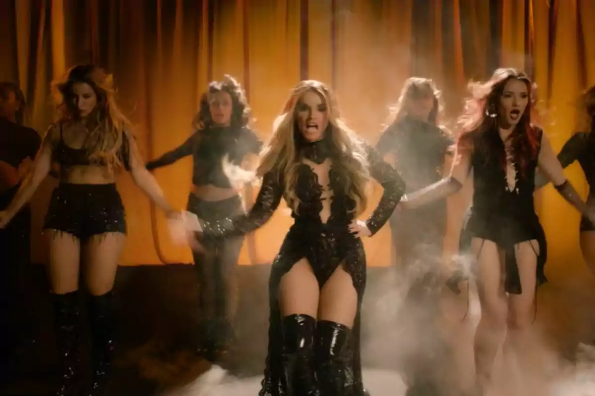 Un grupo de mujeres vestidas con Melody con trajes negros y botas altas realiza una coreografía en un escenario con cortinas doradas y humo en el videoclip de Esa Diva. Un grupo de mujeres vestidas con Melody con trajes negros y botas altas realiza una coreografía en un escenario con cortinas doradas y humo en el videoclip de Esa Diva.