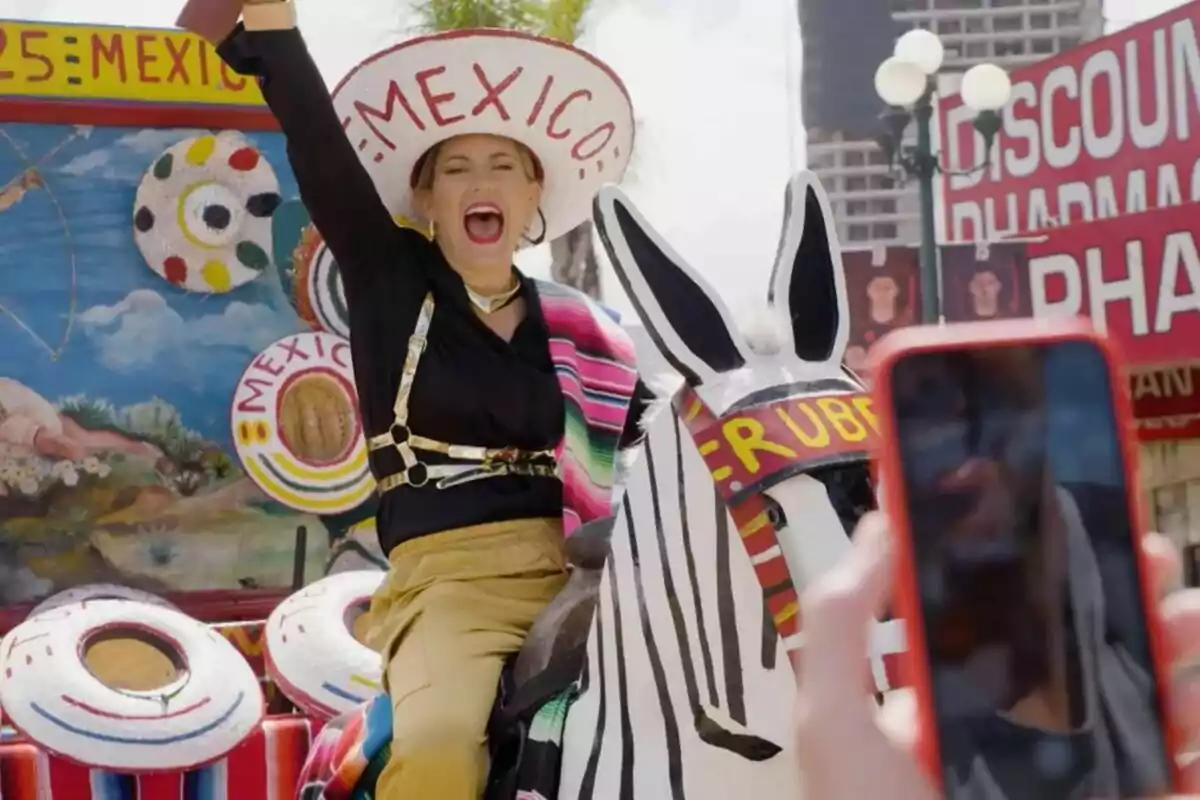 Mujer sonriente con sombrero que dice México montando un burro pintado de cebra en un ambiente festivo mientras alguien toma una foto con el celular