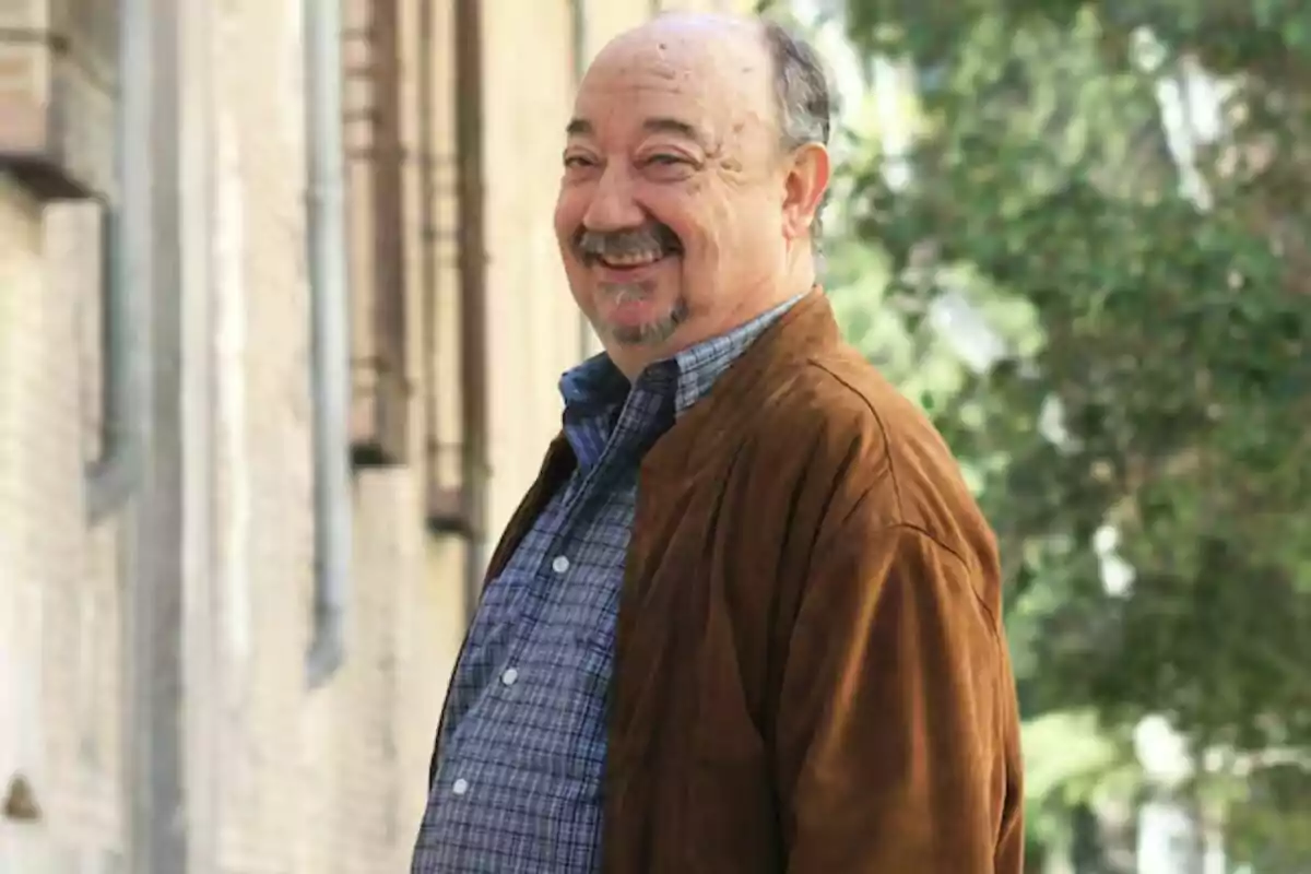 Miguel Vigil sonriendo con una chaqueta marrón y camisa a cuadros, de pie en una calle con árboles y edificios de fondo. Miguel Vigil sonriendo con una chaqueta marrón y camisa a cuadros, de pie en una calle con árboles y edificios de fondo.