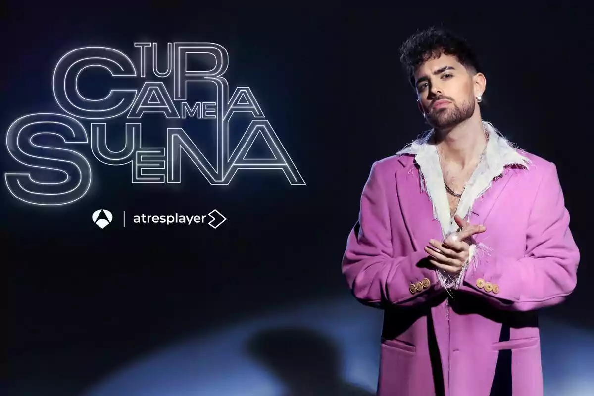 Mikel Herzog JR con barba y cabello rizado lleva un abrigo rosa con detalles de plumas blancas y está de pie frente a un fondo oscuro; a su lado, el texto dice 