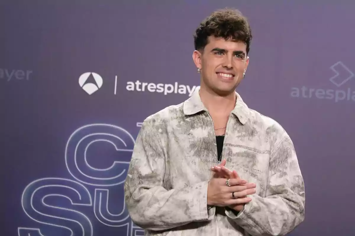 Mikel Herzog Jr con chaqueta clara sonríe frente a un fondo con logotipos de Tu Cara Me Suena, Antena 3 y Atresplayer.