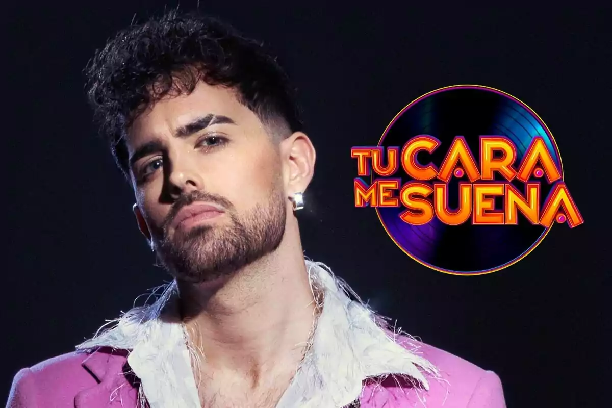 Mikel Herzog Jr con barba y cabello rizado lleva un traje rosa y una camisa blanca, junto al logo del programa "Tu Cara Me Suena".