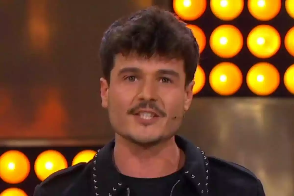 Pla curt de Miki Núñez amb cabell fosc i bigoti parla davant d'un fons de llums taronges que és un plató de TV3. Pla curt de Miki Núñez amb cabell fosc i bigoti parla davant d'un fons de llums taronges que és un plató de TV3.